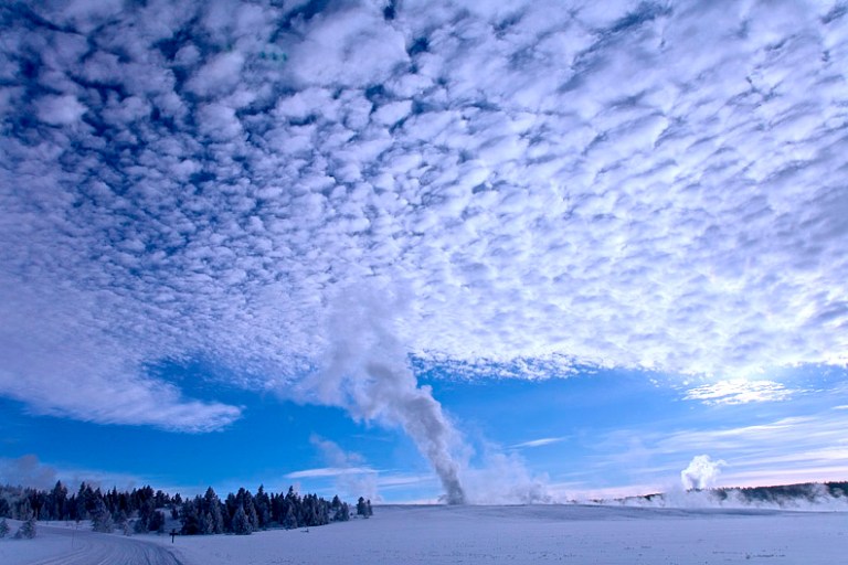 An erupting geyser produces plumes of steam that form a pattern.