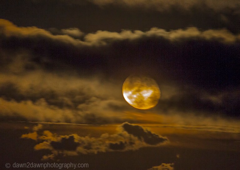 A full moon rises amongst soem passing clouds in Northern Arizona