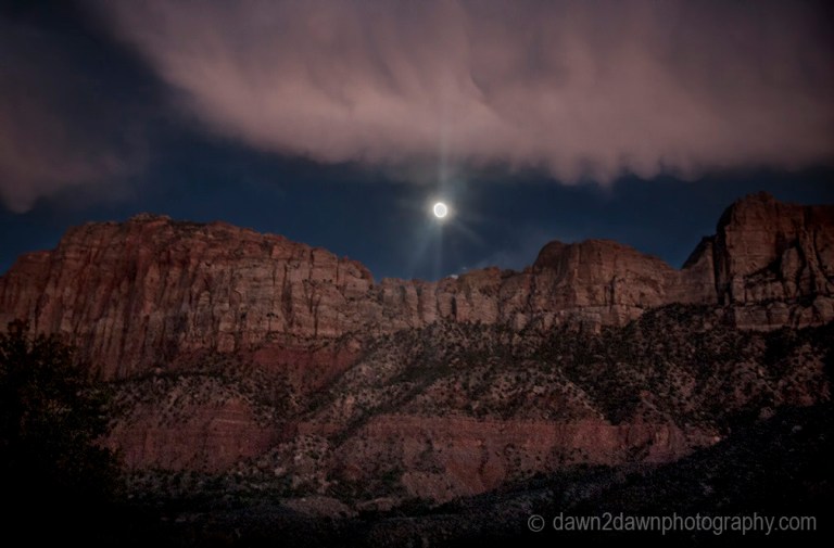 A full moon rises through the clouds and over the rim of Zion Canyon at Zion National Park,Utah